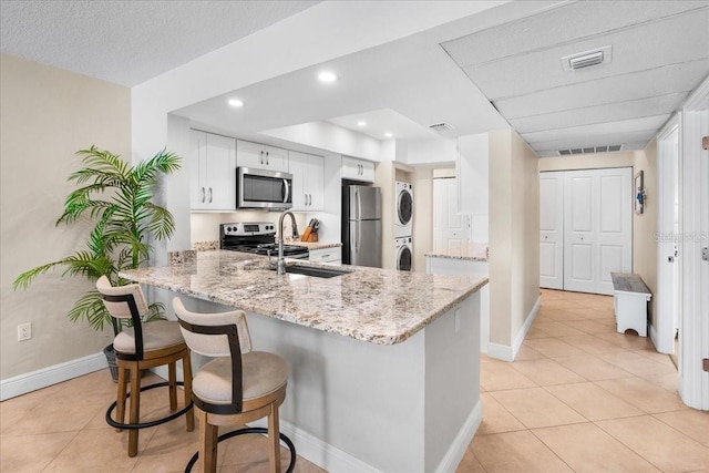 13000 Gulf Blvd Unit 309, Madeira Beach, FL 33708 - kitchen featuring estacked washer and dryer, a peninsula, appliances with stainless steel finishes, light tile patterned flooring, and light stone counters