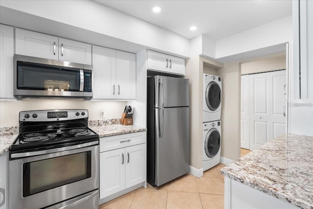 13000 Gulf Blvd Unit 309, Madeira Beach, FL 33708 - kitchen featuring stacked washing machine and dryer, stainless steel appliances, white cabinetry, light tile patterned floors, and light stone countertops