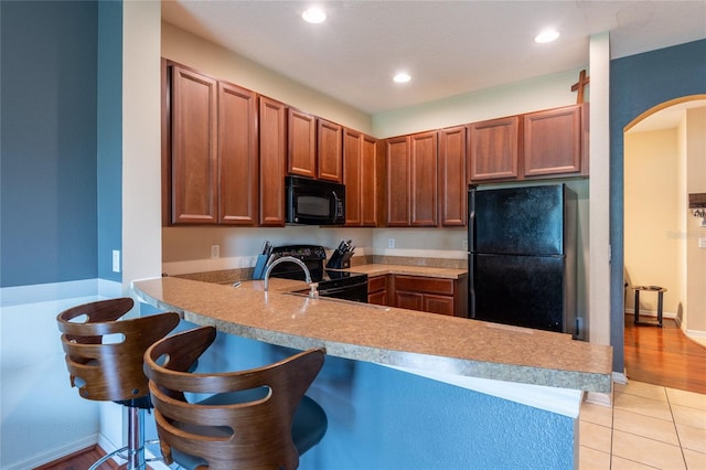 8814 Red Beechwood Ct, Riverview, FL 33578 - kitchen with black appliances, arched walkways, a peninsula, light countertops, and a kitchen bar
