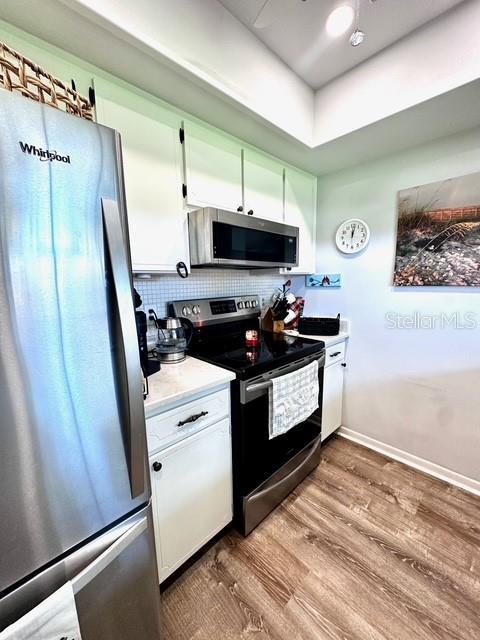 1701 Pinehurst Rd Unit 13C, Dunedin, FL 34698 - kitchen with stainless steel appliances, wood finished floors, light countertops, white cabinets, and decorative backsplash