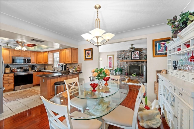 13565 86th Ave, Seminole, FL 33776 - dining room featuring a ceiling fan, a brick fireplace, a chandelier, and light wood finished floors