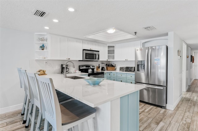 18500 Gulf Blvd Unit 503, Indian Shores, FL 33785 - kitchen featuring stainless steel appliances, a peninsula, light wood-style flooring, a textured ceiling, and white cabinets