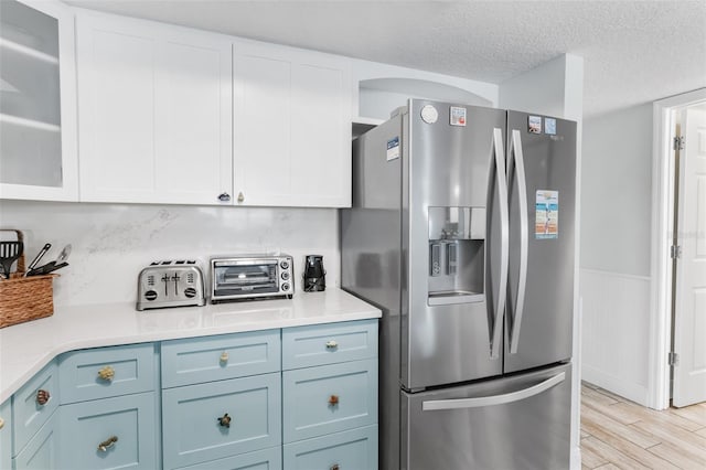 18500 Gulf Blvd Unit 503, Indian Shores, FL 33785 - kitchen with stainless steel refrigerator with ice dispenser, white cabinets, light countertops, light wood-style flooring, and a textured ceiling