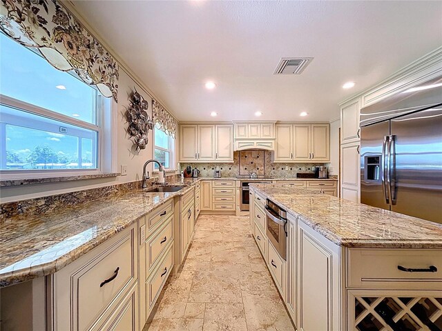 11141 Carla Dr, Largo, FL 33774 - kitchen featuring appliances with stainless steel finishes, a kitchen island, light stone finish floors, light stone countertops, and cream cabinetry