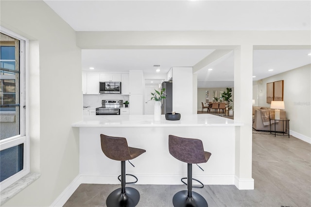 17601 Sterling Ter, Redington Shores, FL 33708 - kitchen featuring stainless steel appliances, white cabinetry, a kitchen bar, a peninsula, and light countertops