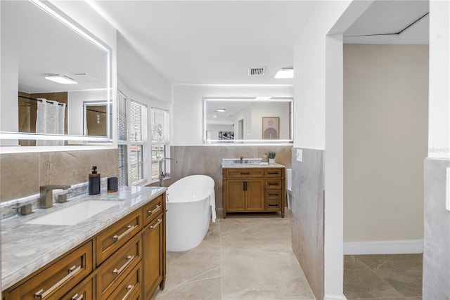 17601 Sterling Ter, Redington Shores, FL 33708 - full bath featuring two vanities, tile walls, a soaking tub, marble finish flooring, and a wainscoted wall