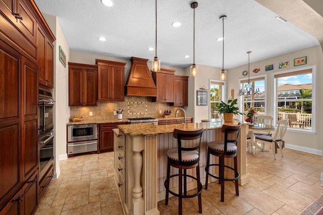 703 Islebay Dr, Apollo Beach, FL 33572 - kitchen featuring custom range hood, backsplash, light stone countertops, a warming drawer, and stainless steel microwave