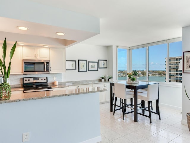 660 Island Way Unit 703, Clearwater Beach, FL 33767 - kitchen with appliances with stainless steel finishes, light stone counters, tasteful backsplash, light tile patterned flooring, and white cabinets
