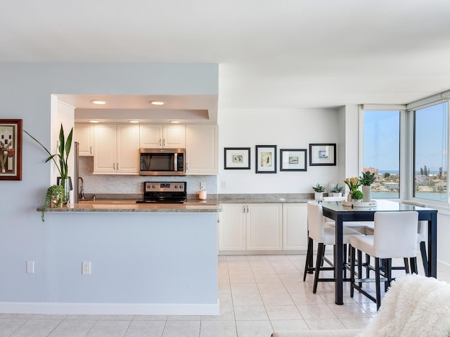660 Island Way Unit 703, Clearwater Beach, FL 33767 - kitchen with appliances with stainless steel finishes, tasteful backsplash, light stone countertops, white cabinetry, and light tile patterned floors