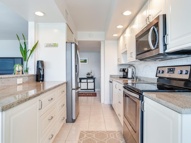 660 Island Way Unit 703, Clearwater Beach, FL 33767 - kitchen with stainless steel appliances, light tile patterned flooring, decorative backsplash, white cabinets, and light stone countertops