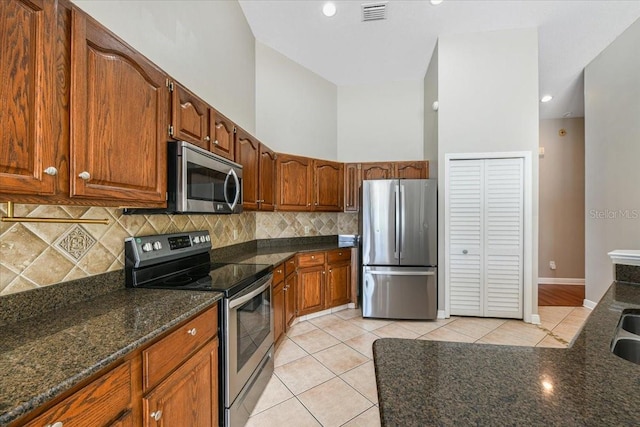 816 Sandringham Ln, Lutz, FL 33549 - kitchen featuring stainless steel appliances, decorative backsplash, light tile patterned flooring, dark stone countertops, and brown cabinetry