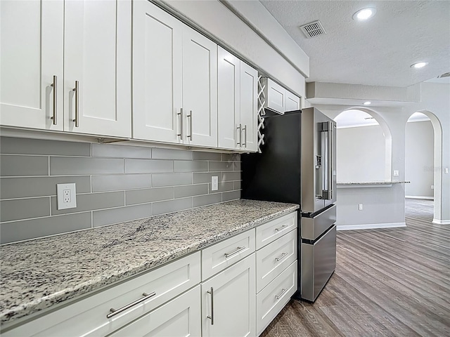 8303 Nightwalker Rd, Weeki Wachee, FL 34613 - kitchen with a textured ceiling, arched walkways, dark wood-style flooring, white cabinets, and stainless steel fridge