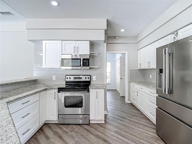 8303 Nightwalker Rd, Weeki Wachee, FL 34613 - kitchen with stainless steel appliances, a textured ceiling, white cabinetry, wood finished floors, and recessed lighting