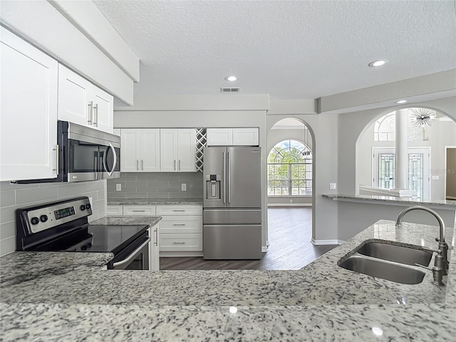 8303 Nightwalker Rd, Weeki Wachee, FL 34613 - kitchen featuring stainless steel appliances, a textured ceiling, arched walkways, dark wood finished floors, and white cabinets