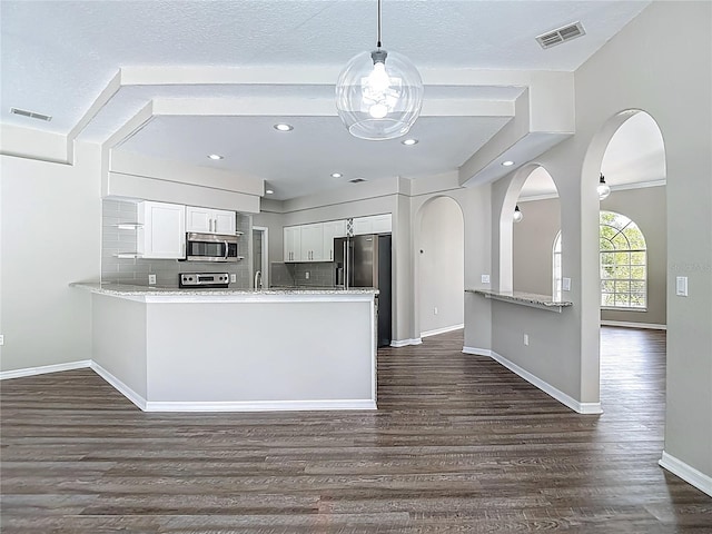 8303 Nightwalker Rd, Weeki Wachee, FL 34613 - kitchen with stainless steel appliances, a peninsula, dark wood-type flooring, white cabinets, and light stone countertops