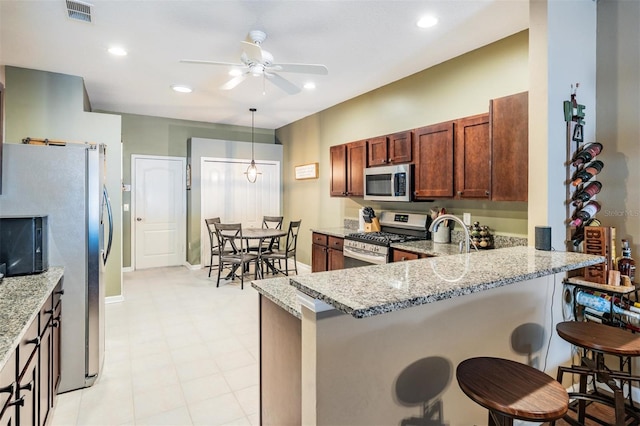 19351 Haskell Pl, Land O Lakes, FL 34638 - kitchen featuring appliances with stainless steel finishes, a ceiling fan, a peninsula, a kitchen breakfast bar, and light stone counters