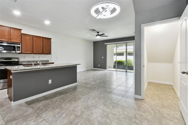 10409 Orchid Mist Ct, Riverview, FL 33578 - kitchen featuring stainless steel appliances, ceiling fan, light stone countertops, a kitchen island with sink, and brown cabinets