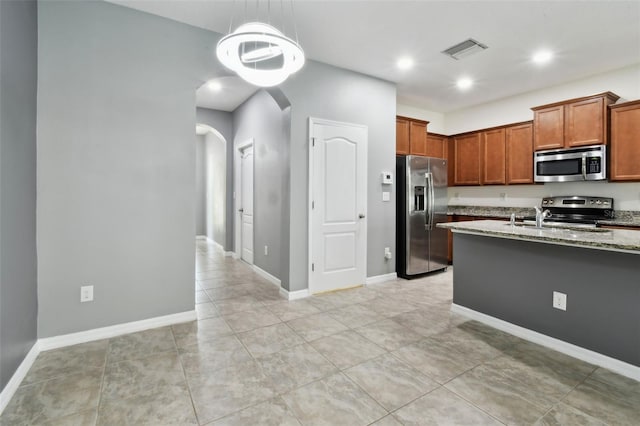 10409 Orchid Mist Ct, Riverview, FL 33578 - kitchen with stainless steel appliances, arched walkways, light stone countertops, hanging light fixtures, and brown cabinets