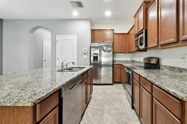 10409 Orchid Mist Ct, Riverview, FL 33578 - kitchen featuring appliances with stainless steel finishes, light stone countertops, brown cabinets, arched walkways, and a center island with sink