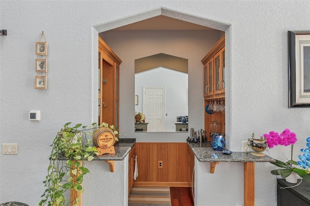5521 Windward Way, New Port Richey, FL 34652 - kitchen with glass insert cabinets, wood finished floors, a wainscoted wall, dark stone countertops, and wood walls