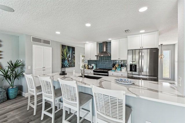11599 Grove St, Seminole, FL 33772 - kitchen with stainless steel fridge, wall chimney exhaust hood, a breakfast bar area, white cabinets, and a textured ceiling