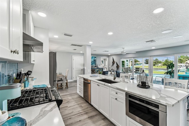 11599 Grove St, Seminole, FL 33772 - kitchen featuring dishwasher, range hood, white cabinets, plenty of natural light, and a textured ceiling