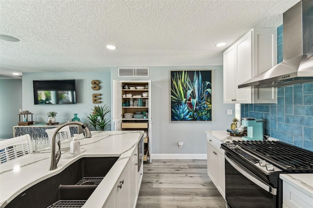 11599 Grove St, Seminole, FL 33772 - kitchen with wall chimney range hood, range with gas cooktop, light wood-style floors, white cabinetry, and decorative backsplash