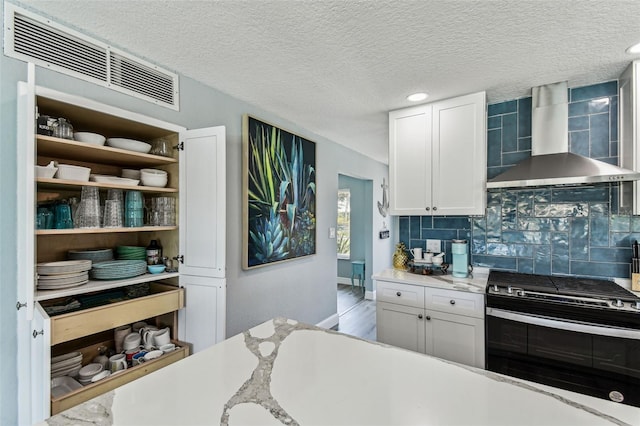 11599 Grove St, Seminole, FL 33772 - kitchen with wall chimney exhaust hood, stainless steel gas stove, backsplash, white cabinets, and recessed lighting