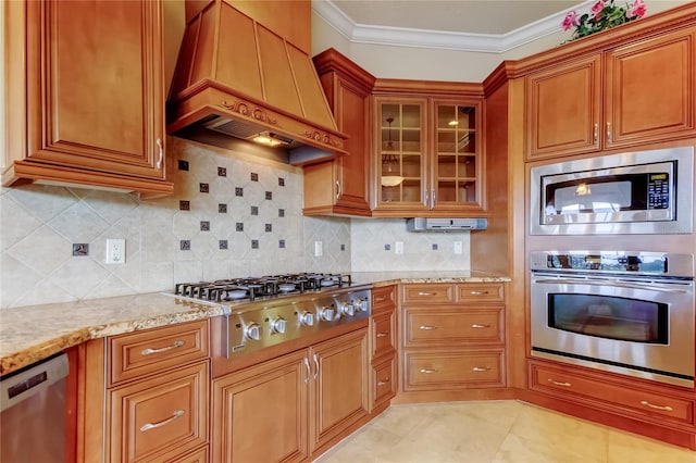 10504 Sabella Dr, Trinity, FL 34655 - kitchen with stainless steel appliances, custom exhaust hood, light stone counters, brown cabinetry, and ornamental molding