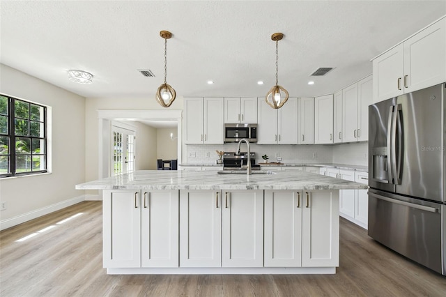 2004 Varner Cir, Winter Haven, FL 33884 - kitchen featuring stainless steel appliances, white cabinetry, light wood-style floors, a center island with sink, and light stone countertops