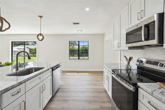 2004 Varner Cir, Winter Haven, FL 33884 - kitchen featuring stainless steel appliances, tasteful backsplash, light wood-style floors, white cabinetry, and pendant lighting