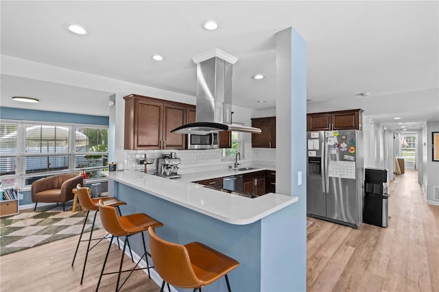 327 Sunny Ln, Belleair, FL 33756 - kitchen featuring stainless steel appliances, light countertops, a breakfast bar, backsplash, and light wood-type flooring