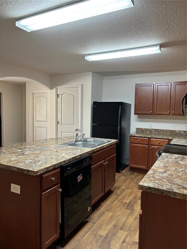 5578 Maggiore Blvd, Lakeland, FL 33805 - kitchen featuring black appliances, light wood finished floors, a textured ceiling, a center island with sink, and arched walkways