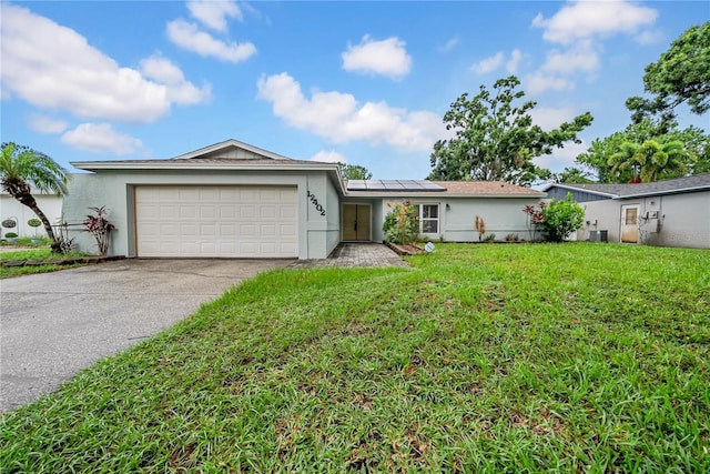 12402 84th Way, Largo, FL 33773 - single story home with stucco siding, a front lawn, roof mounted solar panels, concrete driveway, and a garage
