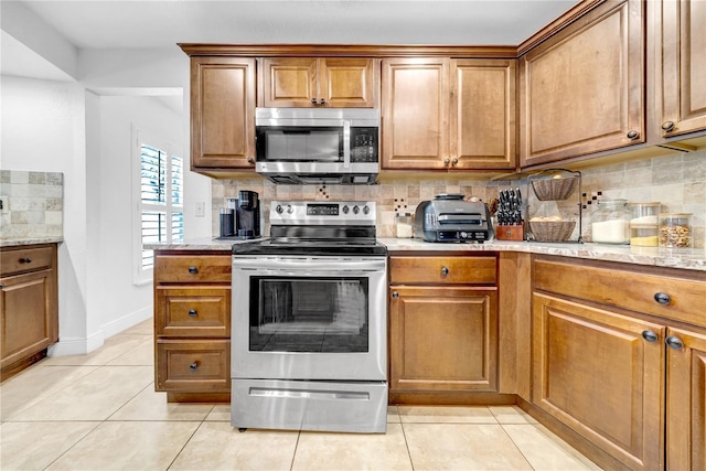 12402 84th Way, Largo, FL 33773 - kitchen featuring appliances with stainless steel finishes, tasteful backsplash, light tile patterned floors, and brown cabinetry