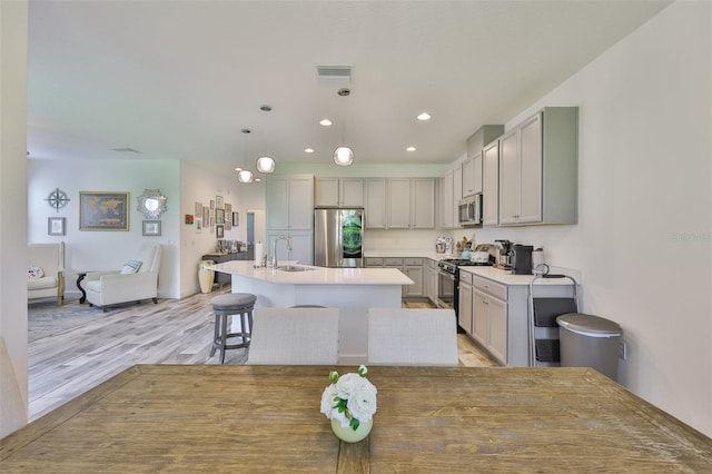 6215 Voyagers Pl, Apollo Beach, FL 33572 - kitchen with appliances with stainless steel finishes, a kitchen island with sink, recessed lighting, light countertops, and light wood-style floors
