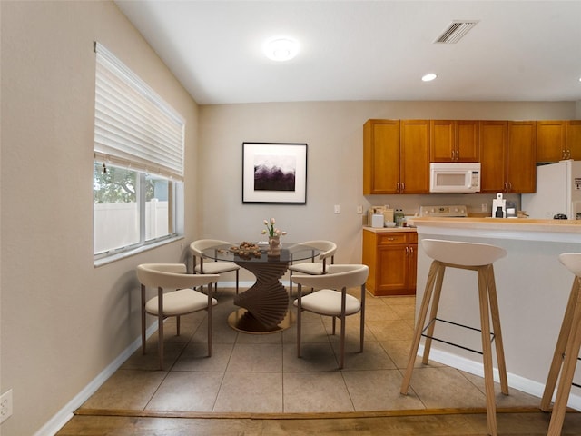 11212 Laurel Brook Ct, Riverview, FL 33569 - kitchen featuring white appliances, brown cabinetry, light countertops, light tile patterned floors, and a kitchen bar
