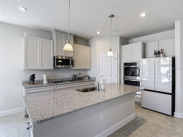 35428 Crescent Creek Dr, Zephyrhills, FL 33541 - kitchen featuring appliances with stainless steel finishes, light stone counters, light tile patterned flooring, a center island with sink, and decorative light fixtures