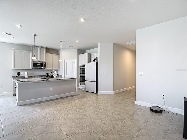 35428 Crescent Creek Dr, Zephyrhills, FL 33541 - kitchen with stainless steel appliances, light stone counters, an island with sink, hanging light fixtures, and a textured ceiling
