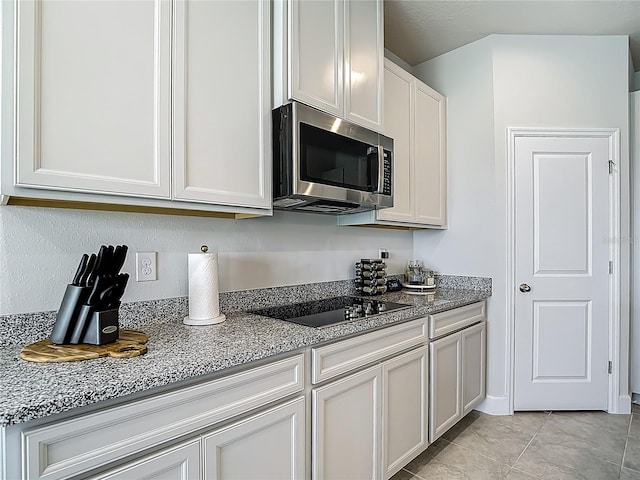 35428 Crescent Creek Dr, Zephyrhills, FL 33541 - kitchen featuring stainless steel microwave, black electric stovetop, light stone countertops, light tile patterned floors, and white cabinetry