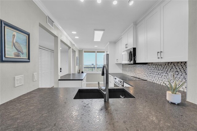 9495 Blind Pass Rd Unit 1103, St Pete Beach, FL 33706 - kitchen featuring dark countertops, appliances with stainless steel finishes, decorative backsplash, white cabinets, and ornamental molding