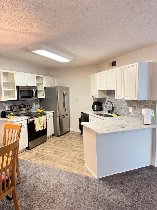 1550 S Belcher Rd Unit 335, Clearwater, FL 33764 - kitchen with appliances with stainless steel finishes, a peninsula, glass insert cabinets, tasteful backsplash, and white cabinets