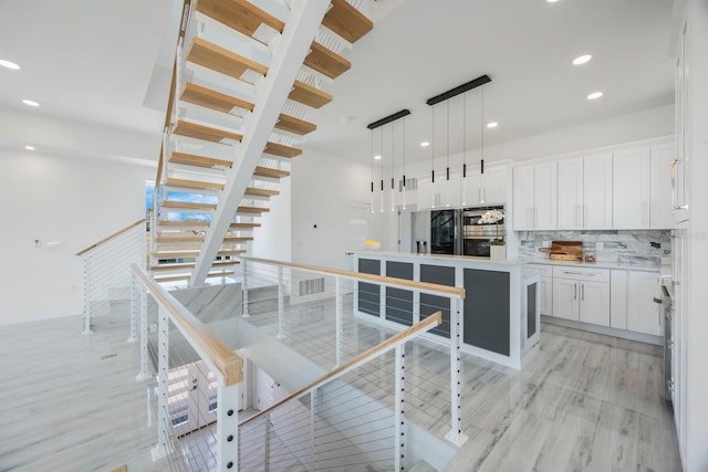 18077 3rd St E, Redington Shores, FL 33708 - kitchen with light wood-style flooring, white cabinets, decorative backsplash, a kitchen island, and light countertops