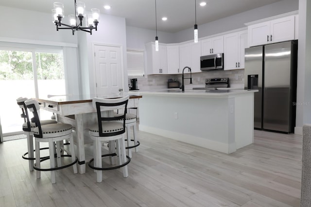 2522 W Castle Rd, Dunnellon, FL 34434 - kitchen featuring appliances with stainless steel finishes, an island with sink, backsplash, light wood-style flooring, and light countertops