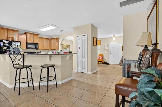 1037 Cypress Pointe Blvd, Davenport, FL 33896 - kitchen with black appliances, a breakfast bar area, light tile patterned floors, arched walkways, and a peninsula