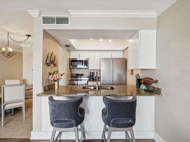 10265 Gulf Blvd Unit A107, Saint Petersburg, FL 33706 - kitchen with stainless steel appliances, a peninsula, crown molding, dark stone countertops, and white cabinetry