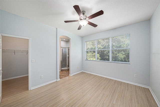 8118 Stone Path Way, Tampa, FL 33647 - unfurnished bedroom featuring arched walkways, a spacious closet, light wood finished floors, a ceiling fan, and ensuite bathroom