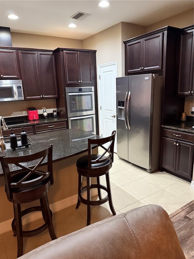 4432 Vermillion Sky Dr, Wesley Chapel, FL 33544 - kitchen featuring stainless steel appliances, a kitchen breakfast bar, dark stone counters, dark brown cabinetry, and recessed lighting