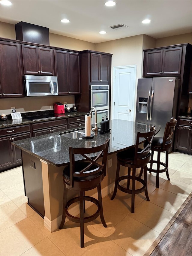 4432 Vermillion Sky Dr, Wesley Chapel, FL 33544 - kitchen with stainless steel appliances, dark stone countertops, a kitchen bar, dark brown cabinets, and a kitchen island with sink