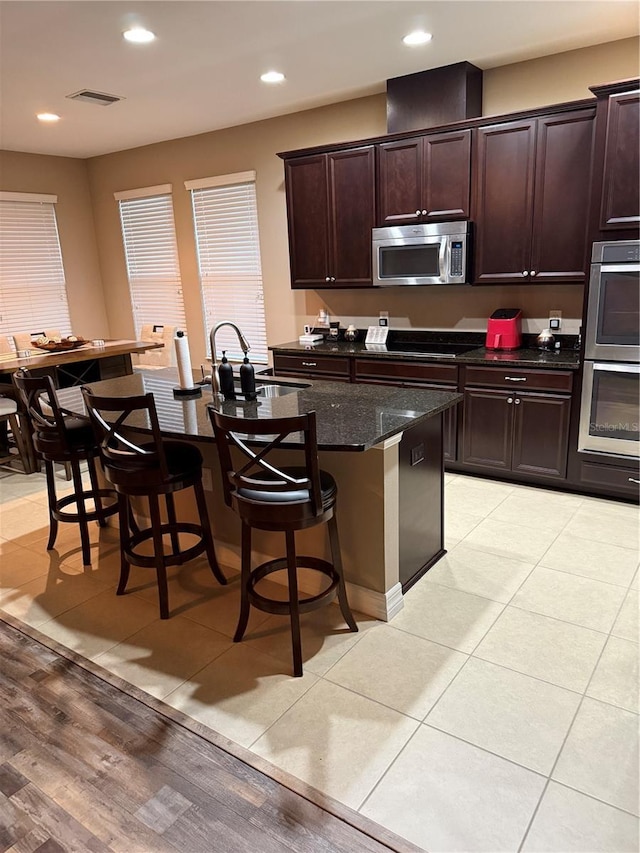 4432 Vermillion Sky Dr, Wesley Chapel, FL 33544 - kitchen with appliances with stainless steel finishes, a breakfast bar area, dark stone counters, recessed lighting, and dark brown cabinetry